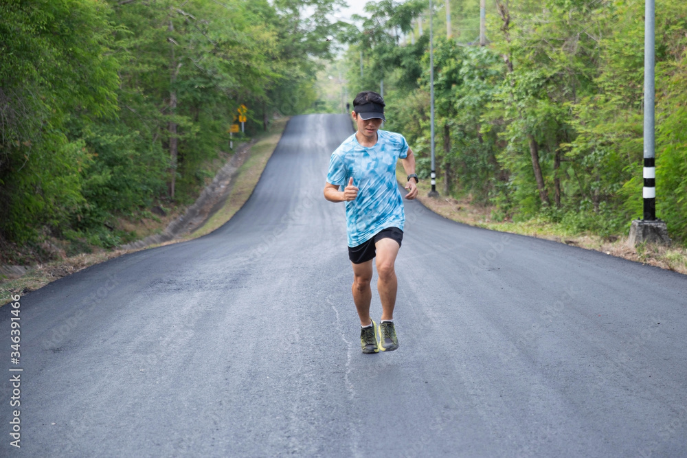 Fototapeta premium The young man runs on the black road in the middle of nature.