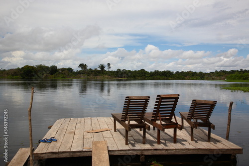 Landscape of Amazon jungle river with floating boat and lodge deck chair on water, Brazil