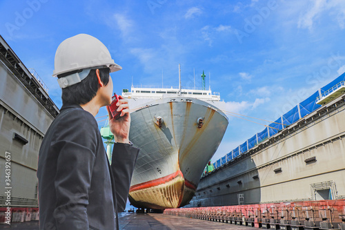 Cargo ship moored in floating dry dock ship repair in Shipyard surveyor controller by walkie talkie in hand, inspecting the final repairing and sandblasting painting on dry dock.