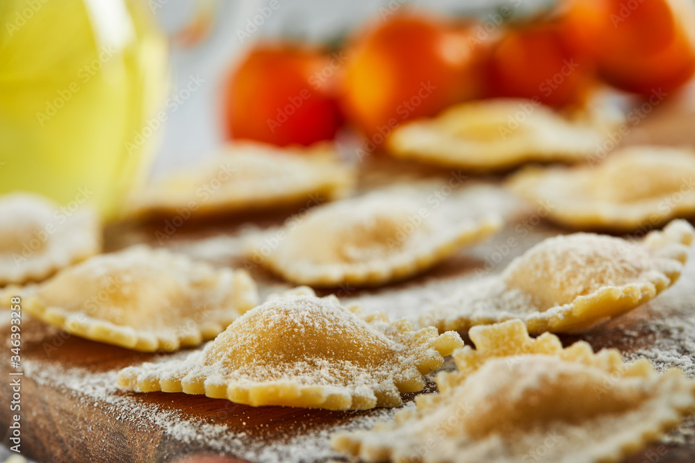 Tasty raw ravioli with flour, cherry tomatoes, sunflower oil and basil on a light wooden background. The process of making Italian ravioli.