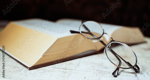 Old hardcover openend  book with vintage retro glasses on a rustic background.  photo