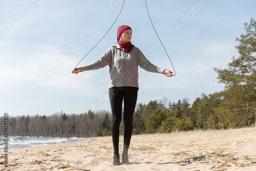 The girl is engaged in sports in nature. exercise with rope, sand and lake.