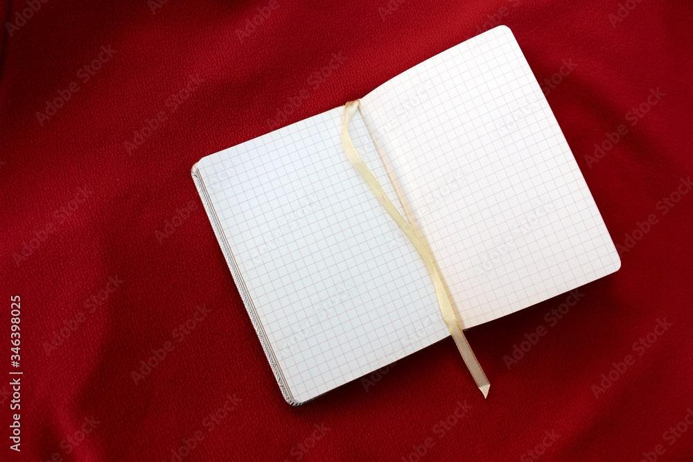 Open notebook on a red background imitating scales. Open notebook in a box on a burgundy background with place for text.