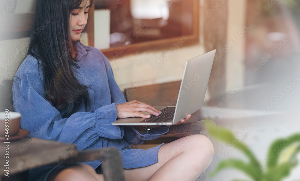 Naklejka premium Young asian woman in casual wear working from home, using laptop while sitting at wooden table in the flower garden with sunlight.