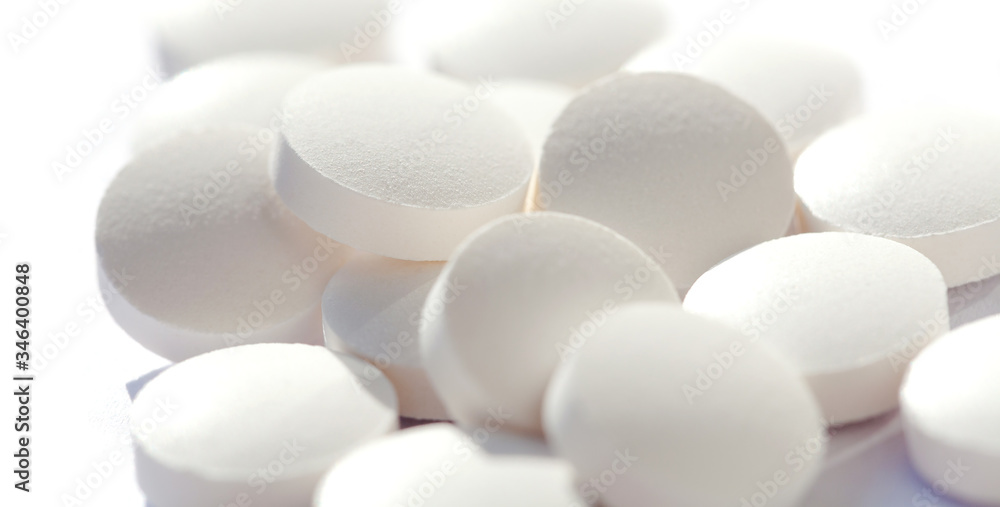 Heap of simple tiny round white pills loose, group of small tablets on white, macro, closeup, focus on one pill. New medicine, supplements and drugs bulk concept. Hi key shot, shallow depth of field