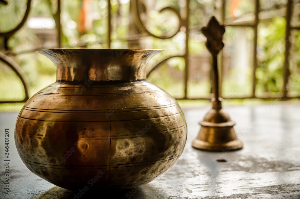 Naklejka premium Close up Still Life of antique Holi water pot and bell on rustic floor. Faith, Tradition, Spirituality, Prayer, symbols of peace and Religious Themes. Arts and culture background concept. Copy space