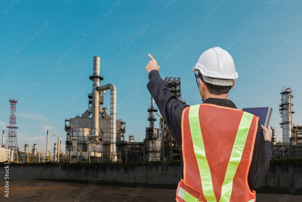 Engineer with tablet in hand wearing safety helmet hand finger pointing for success investment concept with oil refinery industry plant background