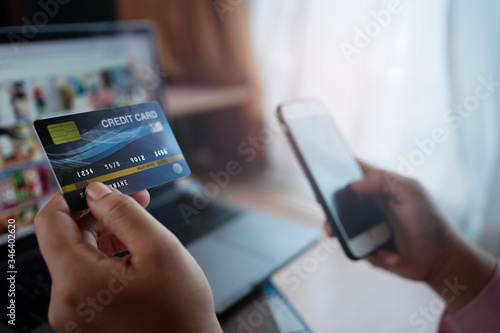 Woman's hands holding a credit card and using laptop and smartphone for online shopping and online payment via internet. Technology concept.