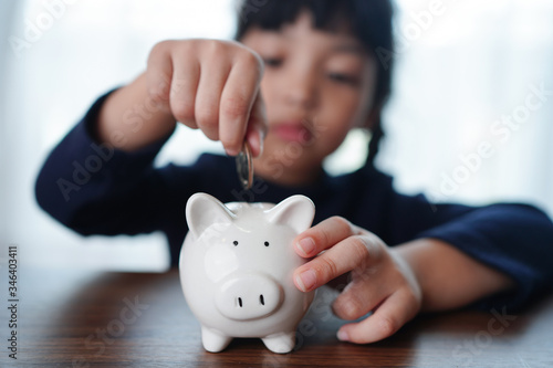 Children's hand puts coins to a white piggy bank. Earnings, saving and finance concept. 