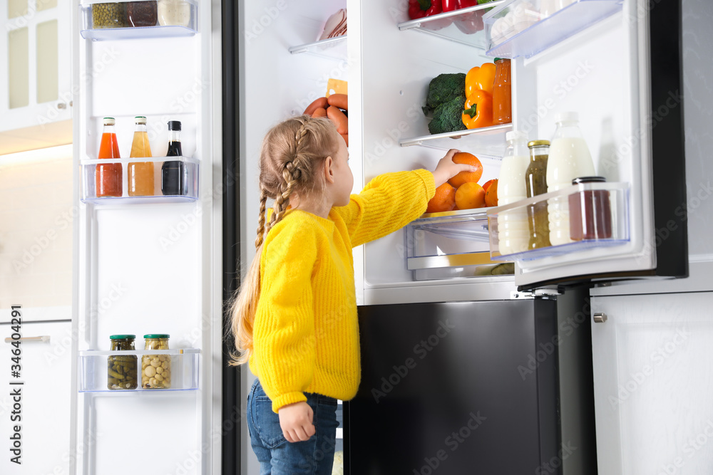 Little girl taking orange out if refrigerator in kitchen Little girl taking orange out if refrigerator in kitchen