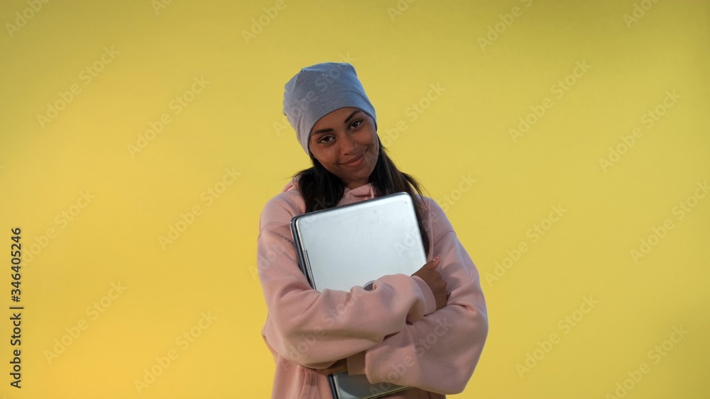 Portrait of African girl in cap hugging her computer laptop and smiling on yellow background. Portrait of African girl in cap hugging her computer laptop and smiling on yellow background.