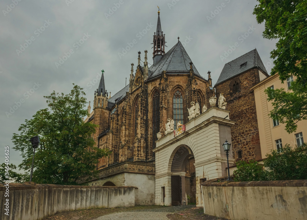 The front arch is decorated with a coat of arms and sculptures, the castle Church with a spire against a cloudy sky. Altenburg Castle. Germany. Soft focus, blurry background.