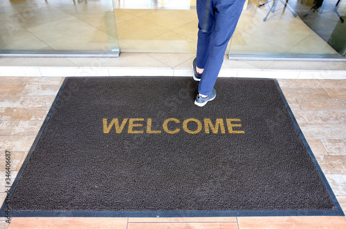 A welcome mat at the entrance of a cafe restaurant as a customer is seen entering through the front door. photo