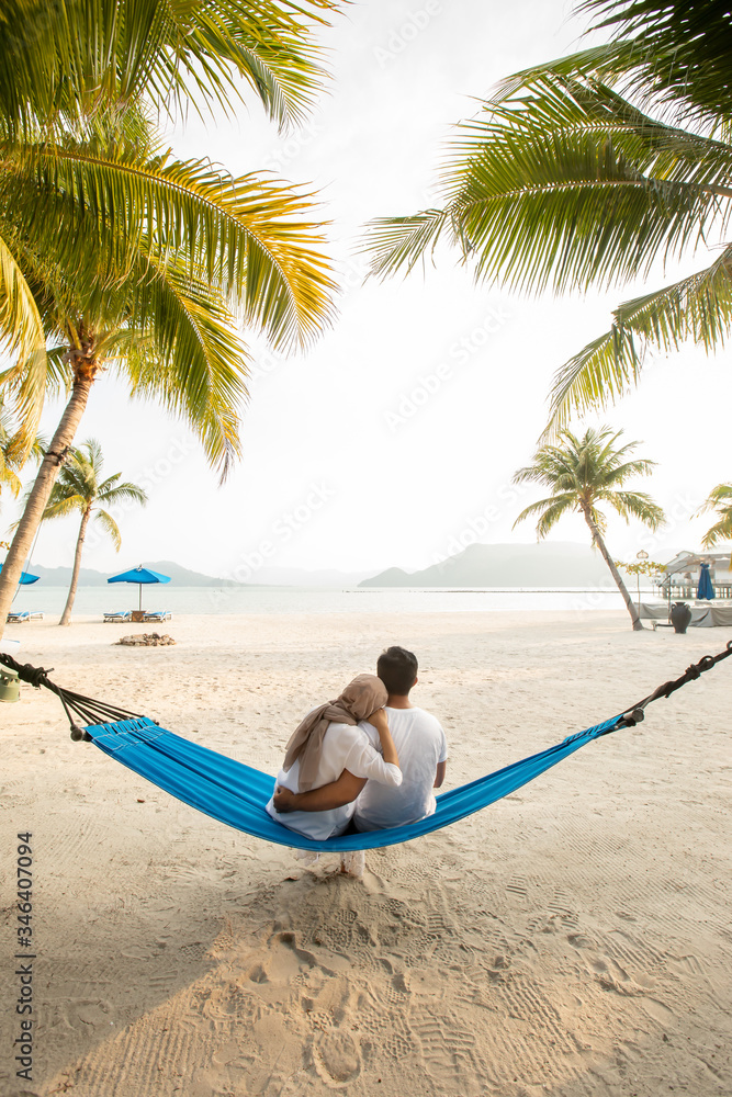 a couple loving hug each other while seating on a hammock at the beach a couple loving hug each other while seating on a hammock at the beach