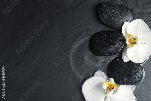 Spa stones and orchid flowers in water on dark background, flat lay with space for text. Zen lifestyle
