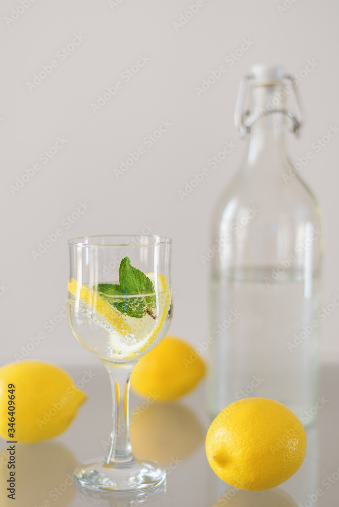 Bottle of cold sparkling mineral water, glass of drink with lemon and mint and whole lemons on glass table. Detox cocktail Bottle of cold sparkling mineral water, glass of drink with lemon and mint and whole lemons on glass table. Detox cocktail