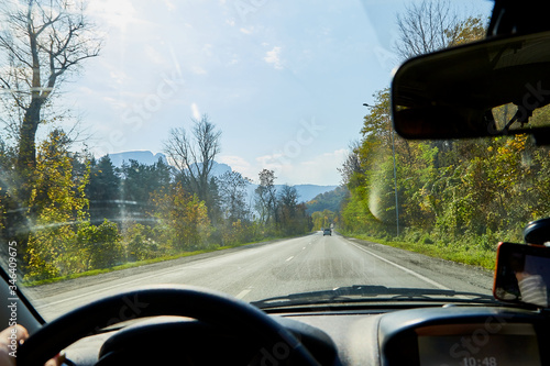 Car salon, steering wheel, hand of woman and view on nature landscape. Road, forest, blue sky at sunny day. Concept of single trip of female traveller and driver during coronavirus