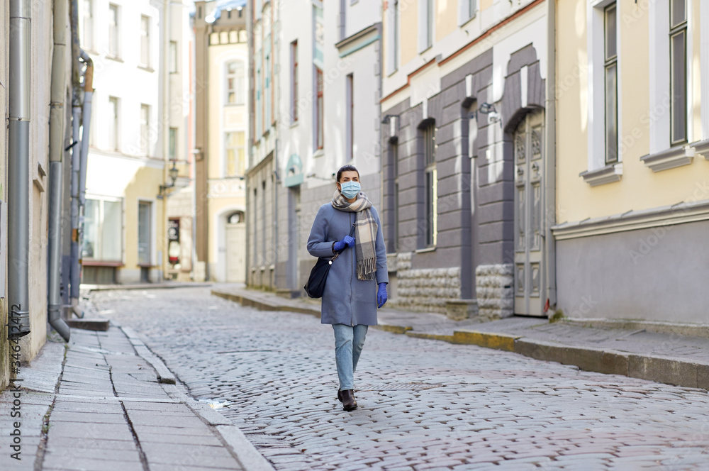 health, safety and pandemic concept - young woman wearing protective medical mask on empty street of old town in tallinn city