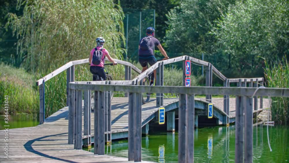 Young couple riding bicycles on wooden pathway and bridge over green water Young couple riding bicycles on wooden pathway and bridge over green water