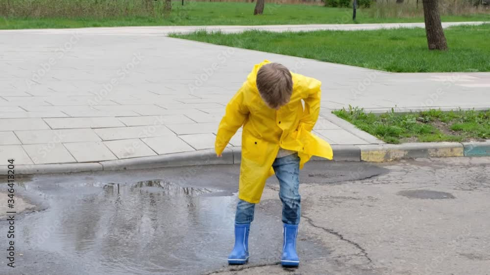 Funny child kid in a yellow raincoat and rubber boots jumping in a puddle Funny child kid in a yellow raincoat and rubber boots jumping in a puddle