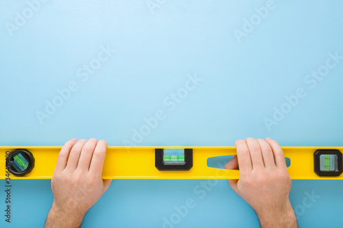 Bild auf Leinwand Man hands holding yellow spirit level on light blue table background
