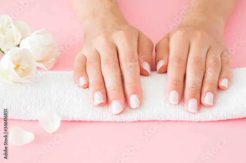 Young  perfect woman hands with white nails on towel. Care about nails and clean  soft  smooth skin. Manicure  pedicure beauty salon. Beautiful roses on pastel pink table. Fresh flowers. Closeup.