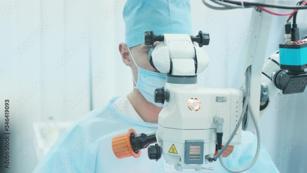 Surgeon looking into the microscope at the eye of female patient at the operating room. Doctor using microscope during eye surgery process, treatment of cataract and diopter correction. Surgeon looking into the microscope at the eye of female patient at the operating room. Doctor using microscope during eye surgery process, treatment of cataract and diopter correction.