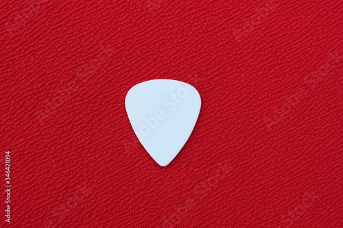 White guitar pick for playing the guitar on a red background. 