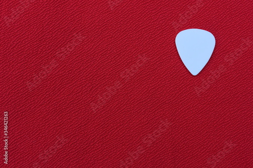 White guitar pick for playing the guitar on a red background. 