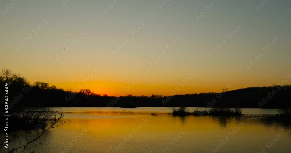 Moving lake surface during an orange sunset on a horizon full of trees and hills behind the lake with reflection on the water surface 4k 60fps Moving lake surface during an orange sunset on a horizon full of trees and hills behind the lake with reflection on the water surface 4k 60fps