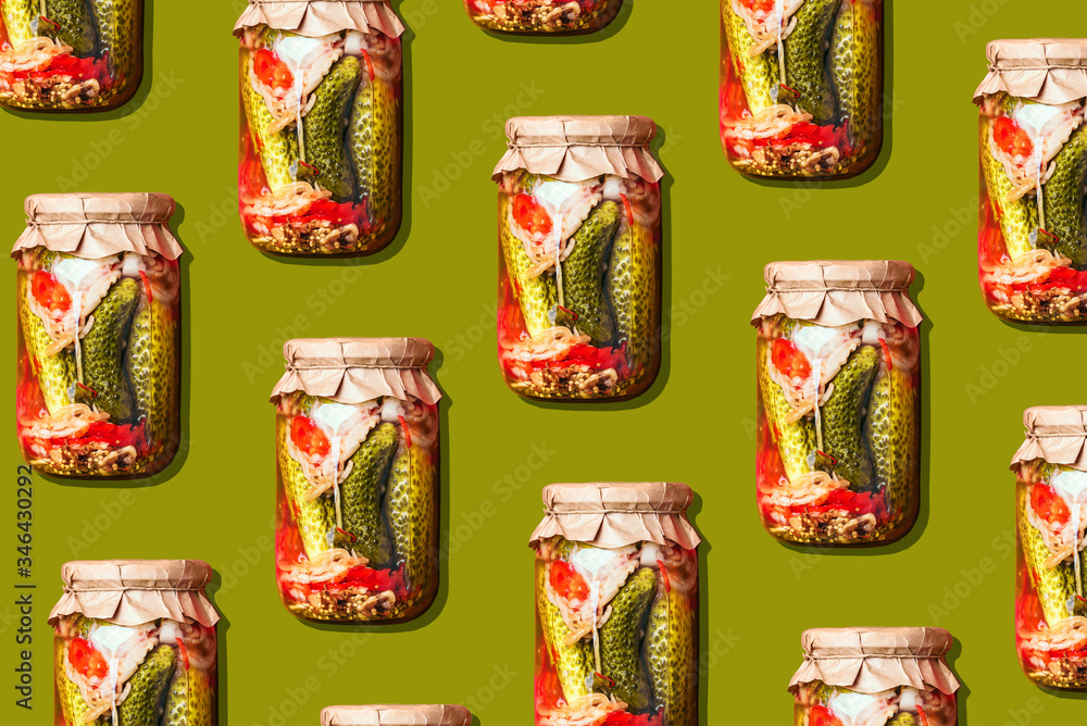 Canned and preserved vegetables in glass jars on green background. Pickled cucumbers in jar pattern. Top view. Flat lay. Creative packing design. Healthy fermented food concept