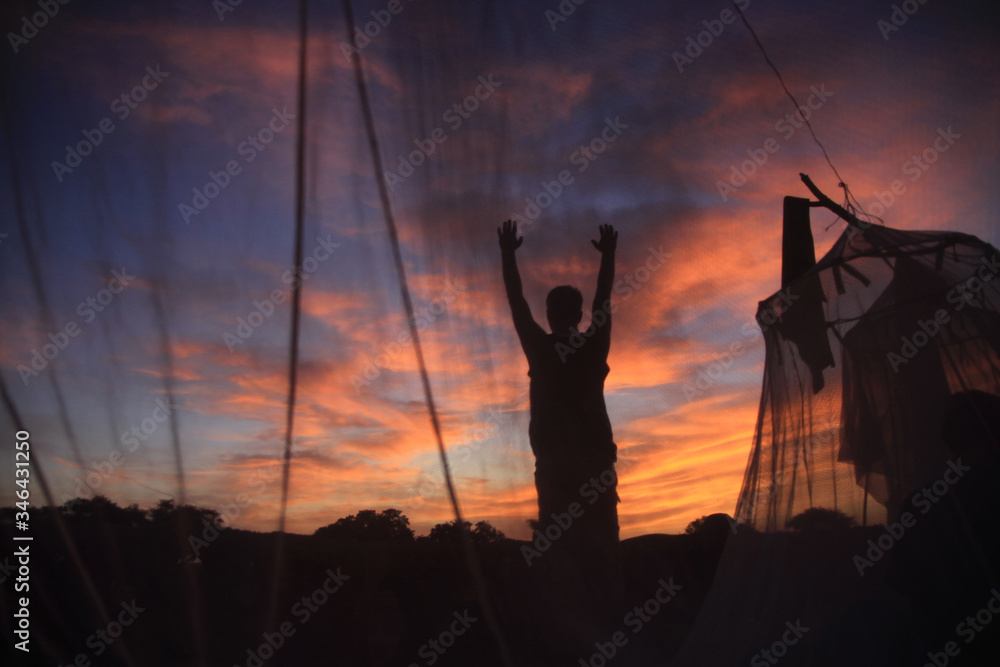 człowiek witający wschód słońca w afryce stojący między namiotami z moskitier - obrazy, fototapety, plakaty 