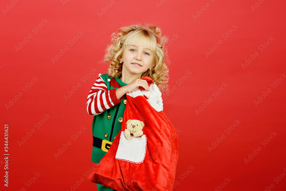 Little girl in Santa elf helper costume on bright red vivid color background.