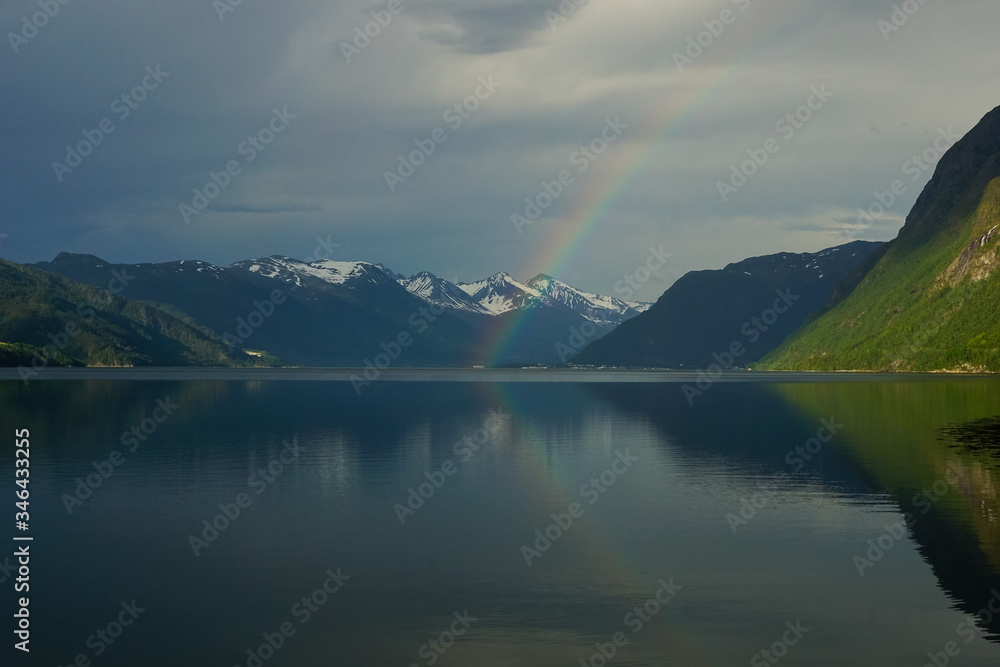 Reflections of mountains and peaks with a rainbow in the waters of Romsdalsfjord in Norway