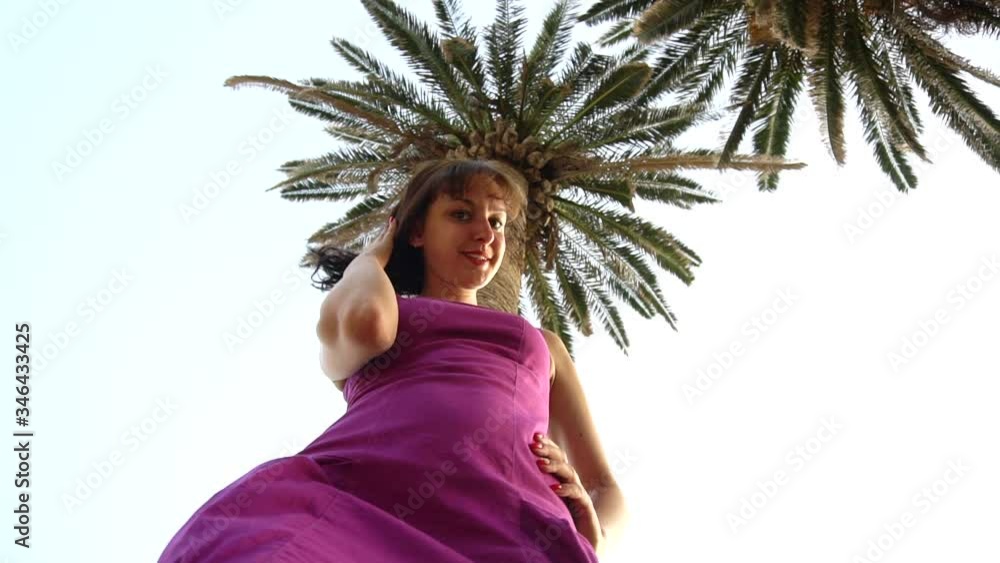 Nice brunette girl looking at the camera on a background of palm trees and blue sky, background, slow motion, caucasian Nice brunette girl looking at the camera on a background of palm trees and blue sky, background, slow motion, caucasian