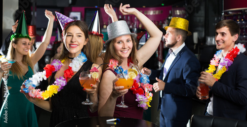 Portrait of young happy women and men in caps with cocktails