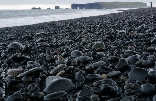 Round pebbles on the seeshore of Reynisfjara beach with a person in the background in Iceland photo