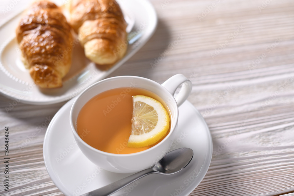 Top view of a cup of tea with lemon and croissant on white table Top view of a cup of tea with lemon and croissant on white table