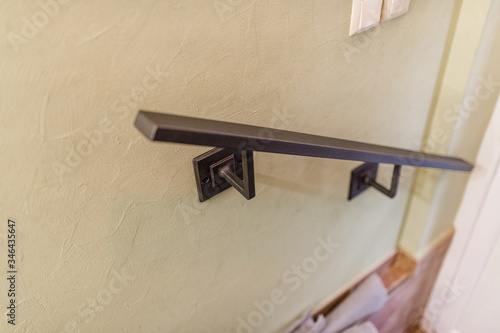 A metal handrail is attached to  light wall original handmade metal mount.