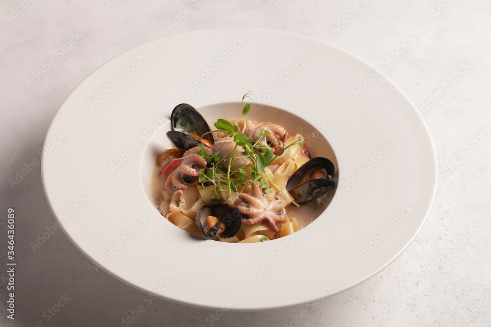 Restaurant menu. pasta with seafood. Octopuses and mussels. Sauce. Micro-greens and cherry tomatoes. White plate. pasta on a white plate