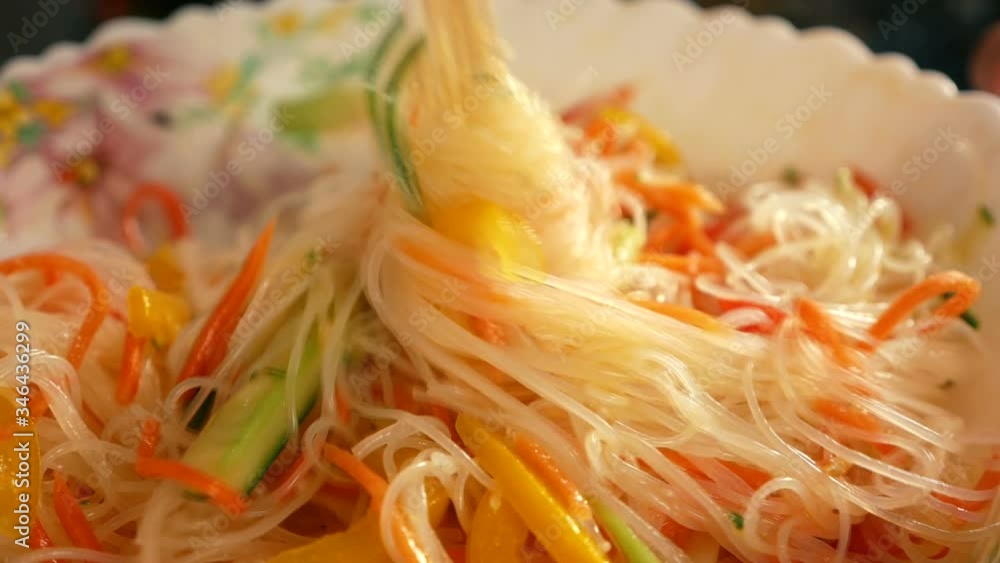 Close-up of chopsticks wrap up appetizing funchoses from a large plate. Asian cuisine and spices Close-up of chopsticks wrap up appetizing funchoses from a large plate. Asian cuisine and spices