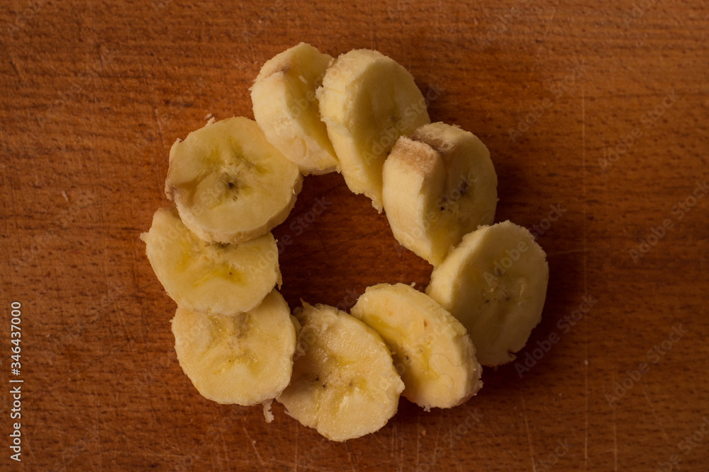 slices of yellow banana laid out in a circle on a wooden board slices of yellow banana laid out in a circle on a wooden board