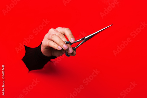 hairdresser holding in hand scissors for cutting hair from a torn hole in red paper
