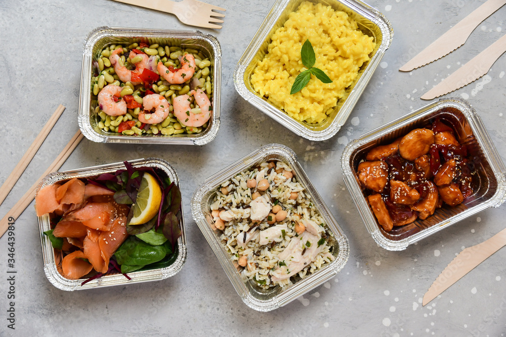 Food delivery. Different aluminium lunch box with healthy food risotto, chicken with chickpeas and rice, salmon and spinach, chicken teriyaki, shrimp and green beans. airline meals snacks. takeaway