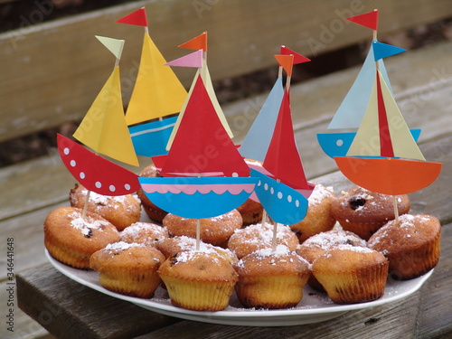  Close-up of sixteen cupcakes on a gravy decorated with colorful paper boats, with a blurred background