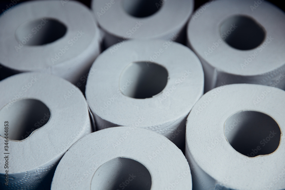 Toilet paper rolls on blue background. Panic shopping during epidemic outbreak time. Light and shadow play with hand reaching towards the toilet paper rolls. Toilet paper rolls on blue background. Panic shopping during epidemic outbreak time. Light and shadow play with hand reaching towards the toilet paper rolls.