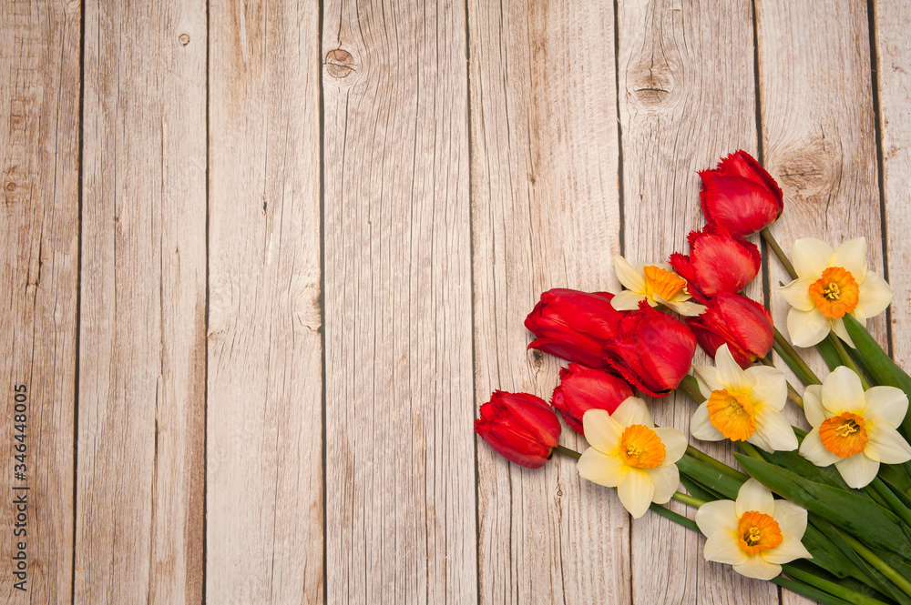 Flower composition. A beautiful bouquet of bright spring red tulips and yellow daffodils on a wooden background. Free space.