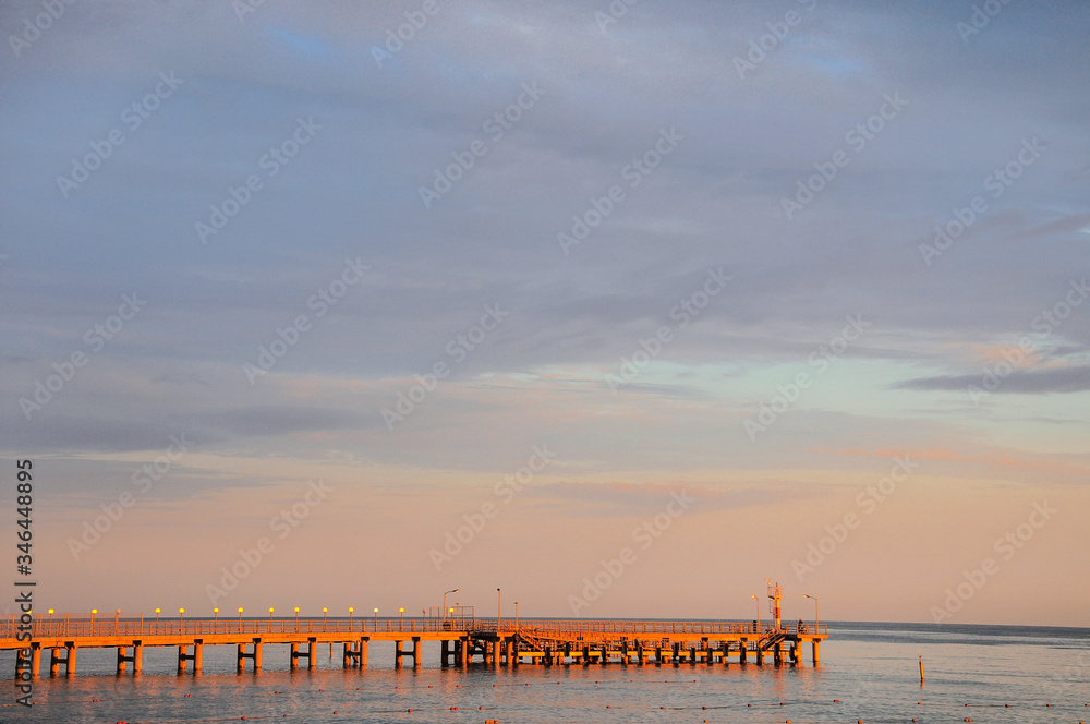 Empty sea pier lit by the sun against the sky.