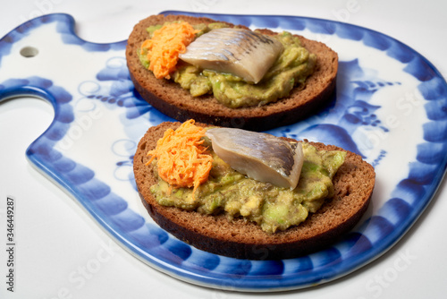 Fresh rye bread with herring and avocado on cutting board