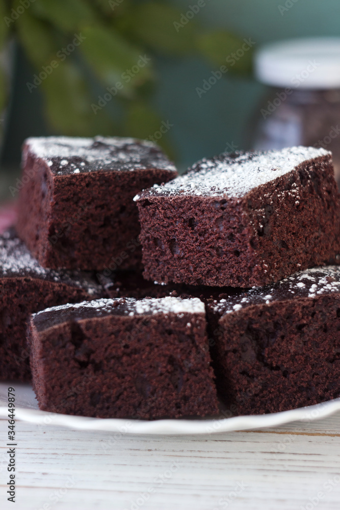 Chocolate cake cut into square pieces, sprinkled with icing sugar on a plate, white background Chocolate cake cut into square pieces, sprinkled with icing sugar on a plate, white background